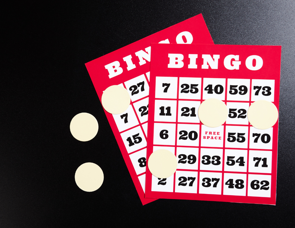 two red BINGO cards with scattered tan tokens on them on a black background
