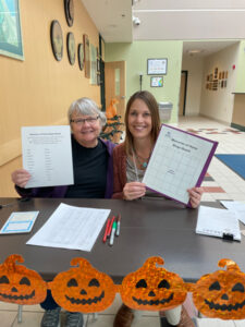 Two people sitting at a greeting table holding up Memory of Home Bingo cards