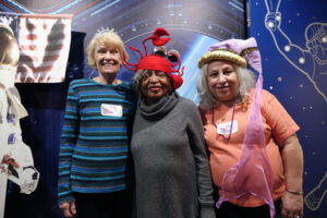 Three older women posing wearing fun, kooky hats