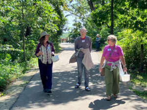 Three people walking on a paved path outdoors on a sunny day