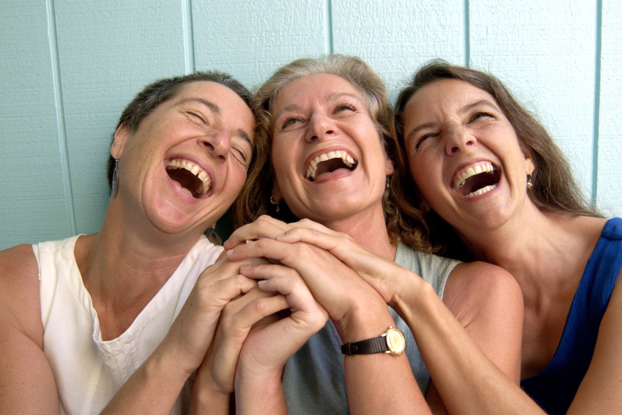 Three women hold hands and laugh at something off camera
