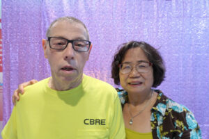 An older woman and an older man smile for the camera in front of a sparkling purple curtain