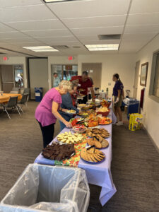A couple people at a table laden with lunch items and desserts.