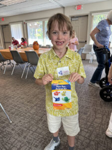 A young boy with a big gap-toothed smile shows off a Pom Pom Animal Kit to the camera.