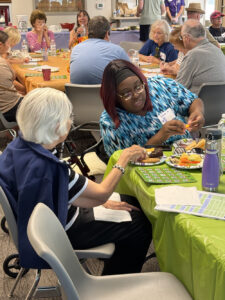 A woman in a blue shirt talks with an older woman at a Memory Cafe.