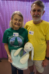 A woman holding a bunny stuffed animal next to a man in a yellow tee shirt smile for the camera.