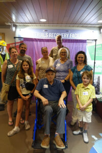 A group of participants at a party post for a party. In the middle is a man in a wheelchair wearing a Brewers baseball cap.