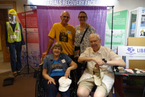 A family of four older adults pose in front of a purple screen for a party.