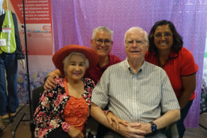 A group of four people pose in front of a purple party screen.
