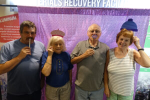 A group of four older adults pose in front of a purple curtain with silly