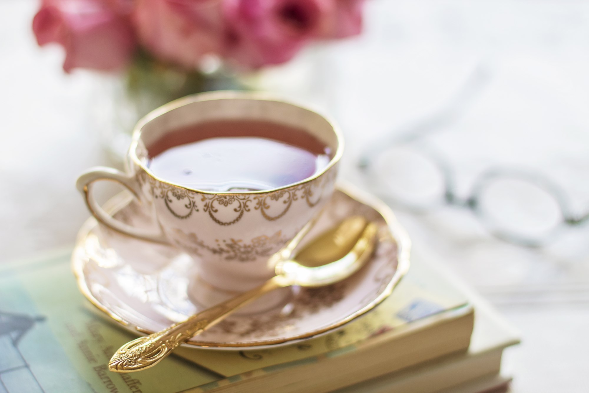 Close up of a white tea cup with gold filligree filled with tea and sitting on top of a stack of books.