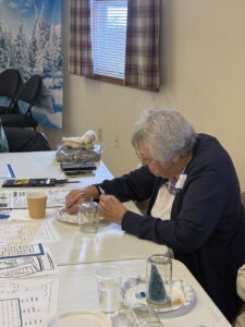 A woman in a black cardigan works on a craft at a table.