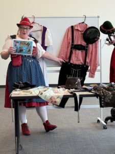 A woman wearing lederhosen presents articles of traditional Swiss clothing.