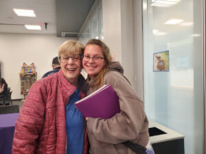A young woman and an older woman pose for the camera with an arm around the other.