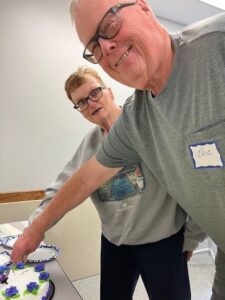A man and woman smile for the camera as they cut a cake.
