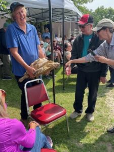 A man in a blue polo shirt is very happy to carry a turtle at an outdoor presentation event.