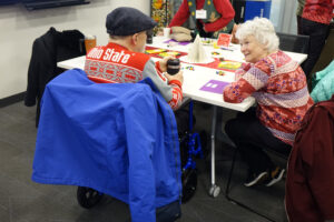 A woman and man in holiday sweaters at a table at a Memory Cafe.