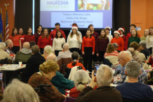 A high school choir sings holiday carols at a well-attended Memory Cafe.