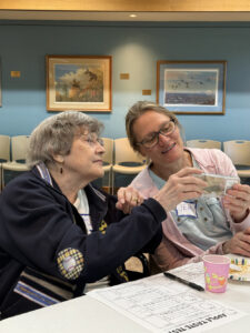 Two women hold a handheld game as they play it together.