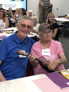 A woman in pink holds a ukelele next to a man in a blue polo