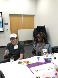 An older man and a woman smile as they shake shakers for a music-themed Memory Cafe.