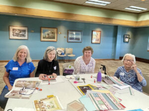 A group of four women smile for the camera at a Memory Cafe where they make a paper collage.