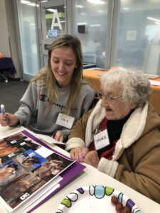 A young woman named Josi helps an older woman named Caroline identify animals on a sheet of paper.