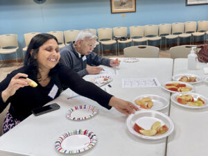A woman in black places a plate of sliced apples on a table.