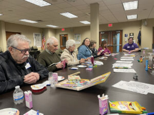 A group of Memory Cafe participants sit at a table for a Valentine's Day themed activity