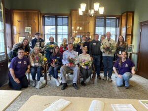 A group photo of Memory Cafe participants holding bouquets of flowers.