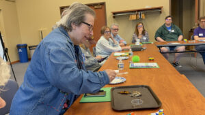 A woman in a denim shirt inspects a tray with a couple butterflies on it.