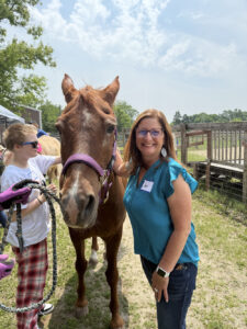 A woman in a nice blue blouse poses next to a friendly horse.