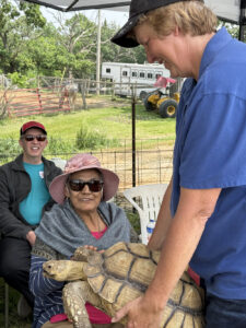 A woman pets a large turtle held by a man in a blue polo shirt