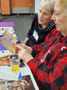 A woman in a buffalo plaid shirt shows an acrylic craft to a woman in a black sweater.