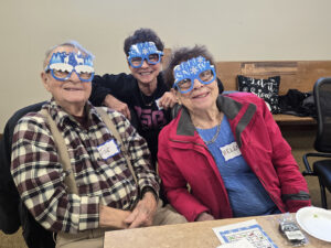 Two elderly women and an elderly man show off their fun snow day glasses with big smiles.