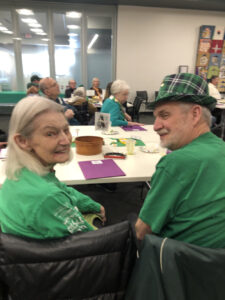A woman and man wearing green turn over their shoulders to smile at the camera.