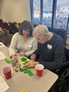 A woman with the name tag Lori helps a man with the name tag Al with a set of legos.