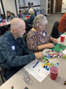 A man in a blue collared shirt helps a woman in a floral shirt construct something with legos.