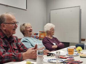A trio of Memory Cafe participants laugh at something to the right of the frame.