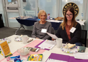 Two women at an event table smile for the camera.