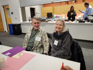 An older couple smile for the camera at a memory cafe event.