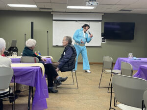An Elvis impersonator passionately sings into a microphone while the audience watches on.