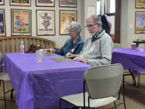 An older couple plays bingo at a table in a purple tablecloth.