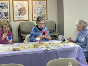 A group of three older women paint bird houses at a memory cafe event.