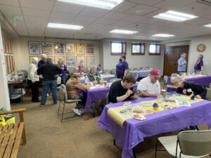 People gather around tables and friends at an event for the Library Memory Project where participants paint bird houses