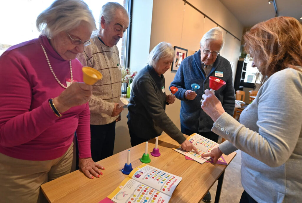 Elderly people standing around a table holding strange cups that are part of a game