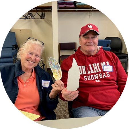 Two people holding up feathers they crafted out of paper