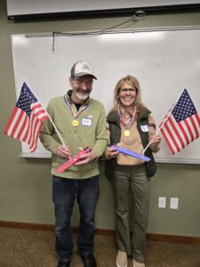 Two people holding American flags and toy planes, wearing gold medals.