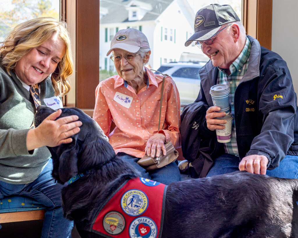 Two people look on as a dog handler pets her therapy dog