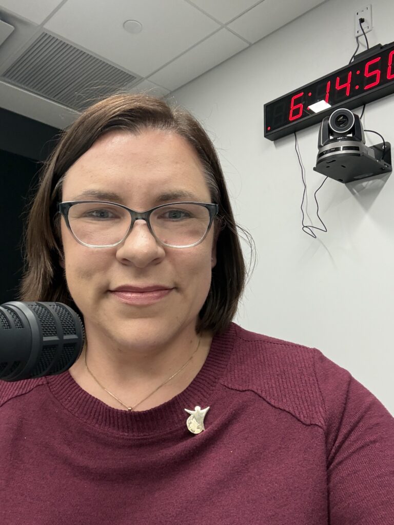 Woman sits in a sound booth at a radio station in front of a microphone